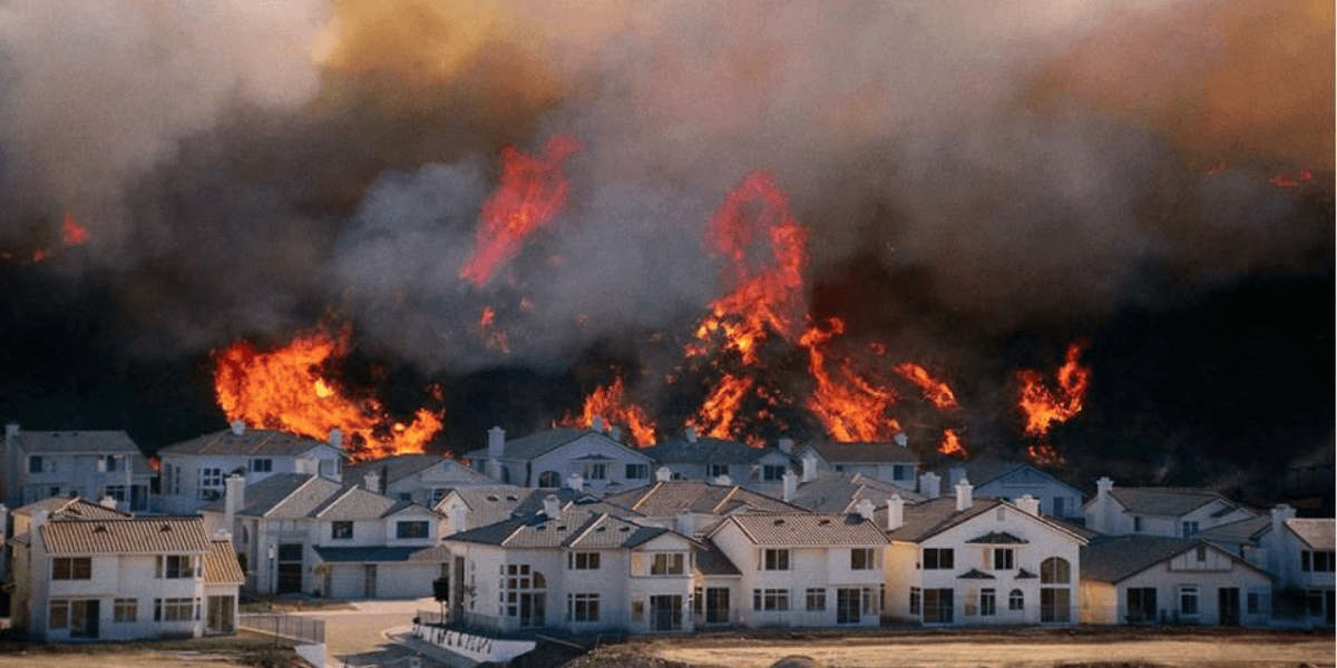 Wildfire engulfing a residential area with flames and smoke looming over homes