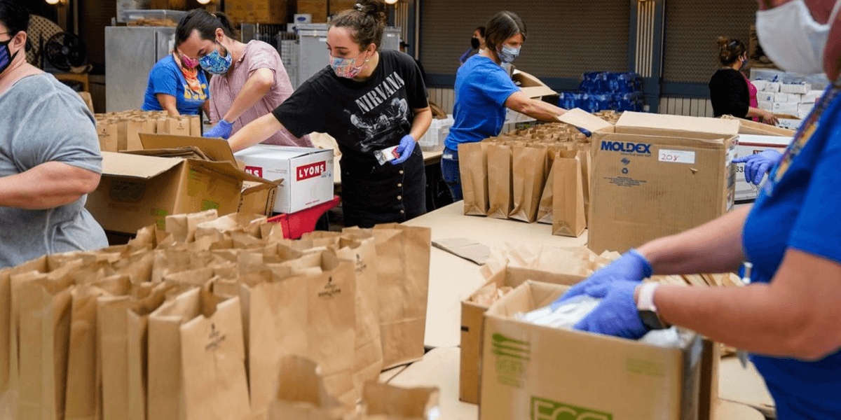 Volunteers packing food items into bags for distribution in a warehouse setting