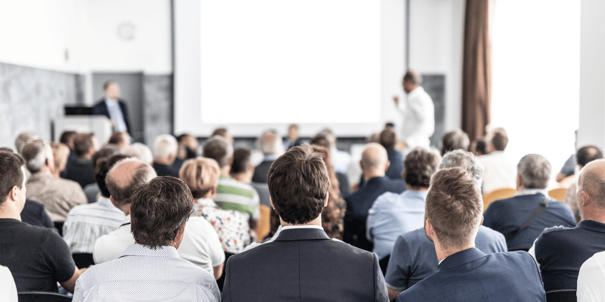 Audience facing a speaker at a presentation in a well-lit room