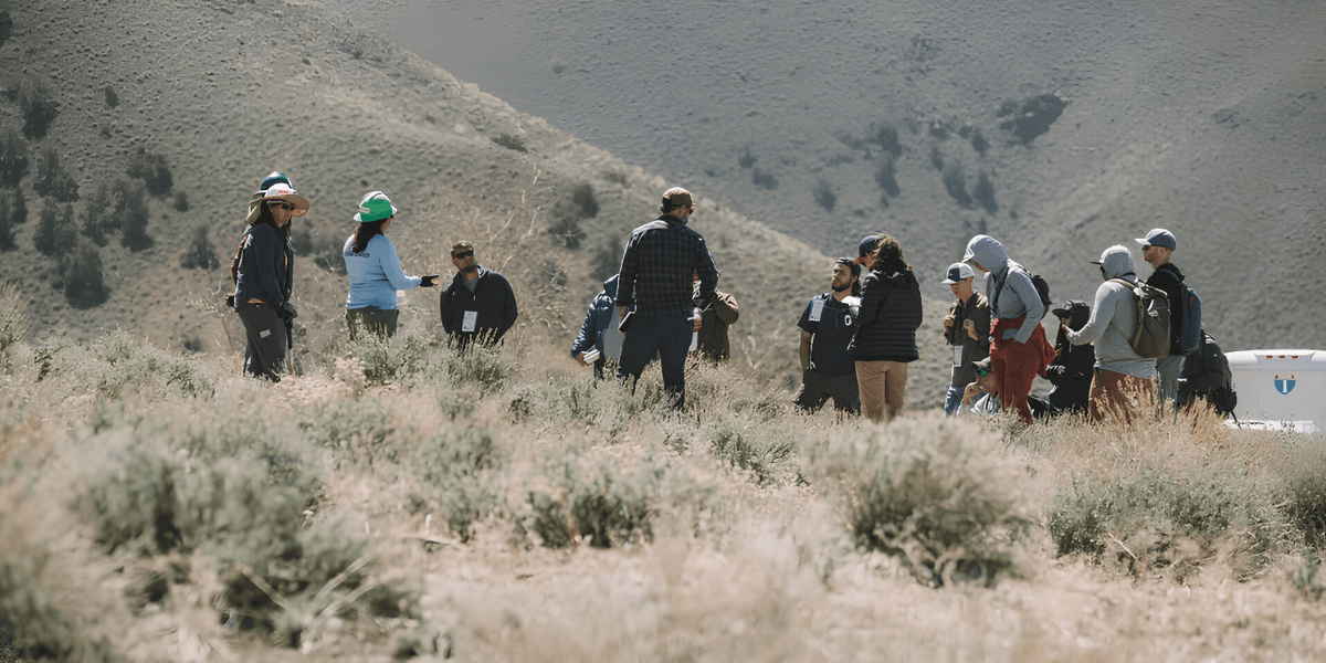 Group of people gathered outdoors in a mountainous area, engaging in discussion.
