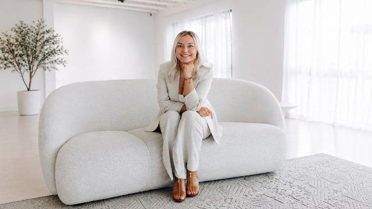 Josey Lesmeister seated on a white sofa in a bright studio.