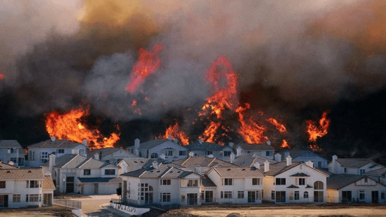 Wildfire engulfing a residential area with flames and smoke looming over homes