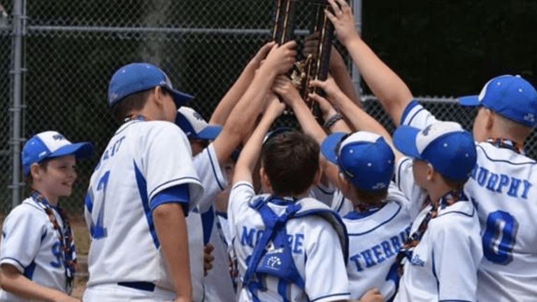 Children in baseball uniforms celebrate while lifting a trophy together