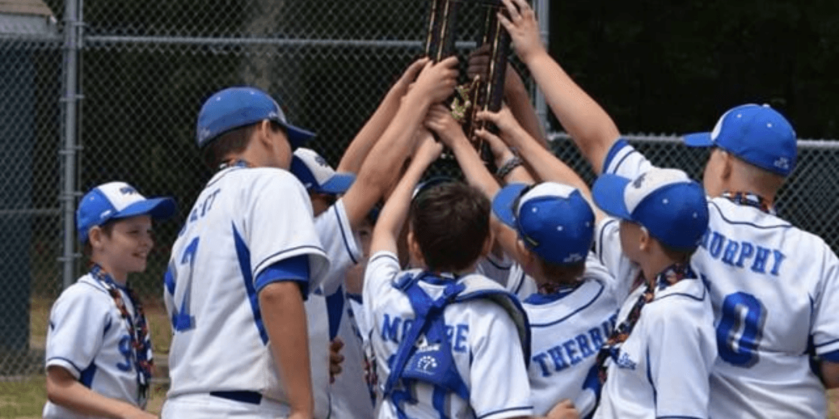 Children in baseball uniforms celebrate while lifting a trophy together