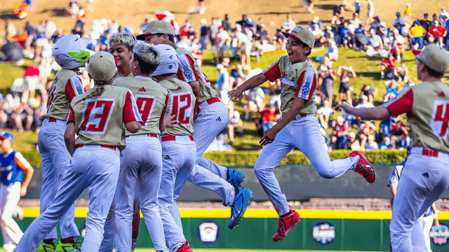Young baseball players celebrating a victory on the field with fans in the background
