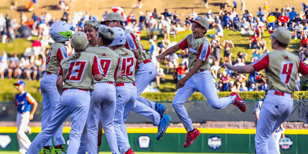 Young baseball players celebrating a victory on the field with fans in the background