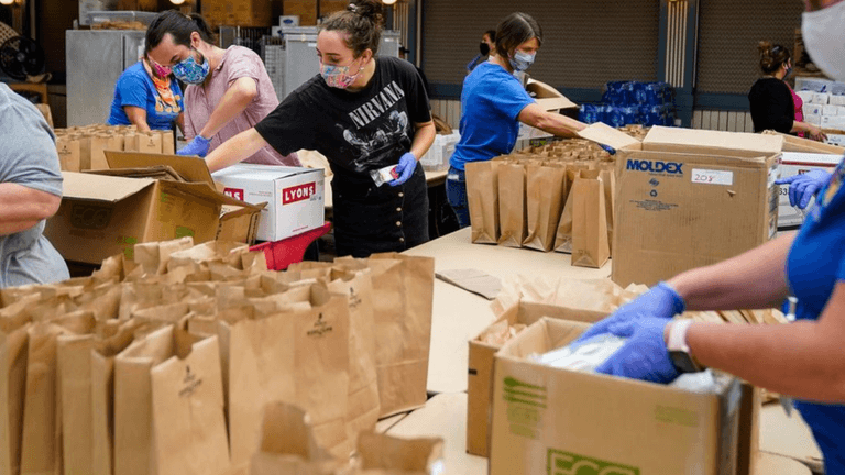 Volunteers packing food items into bags for distribution in a warehouse setting