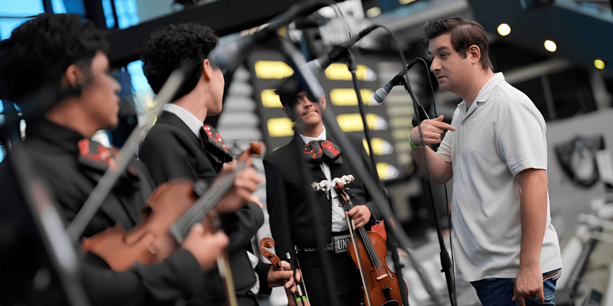 A man speaks to a mariachi band performing indoors with instruments in hand