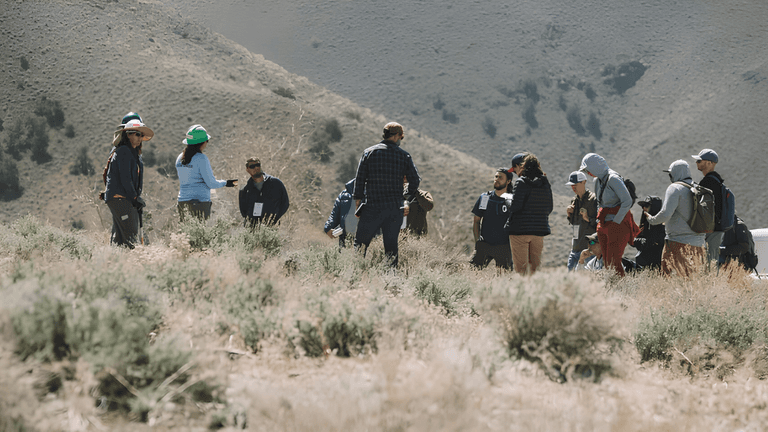 Group of people gathered outdoors in a mountainous area, engaging in discussion.