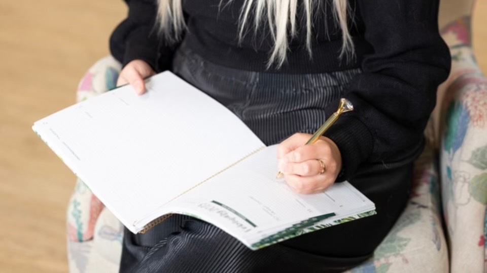 Person writing in a planner while seated in a patterned chair.